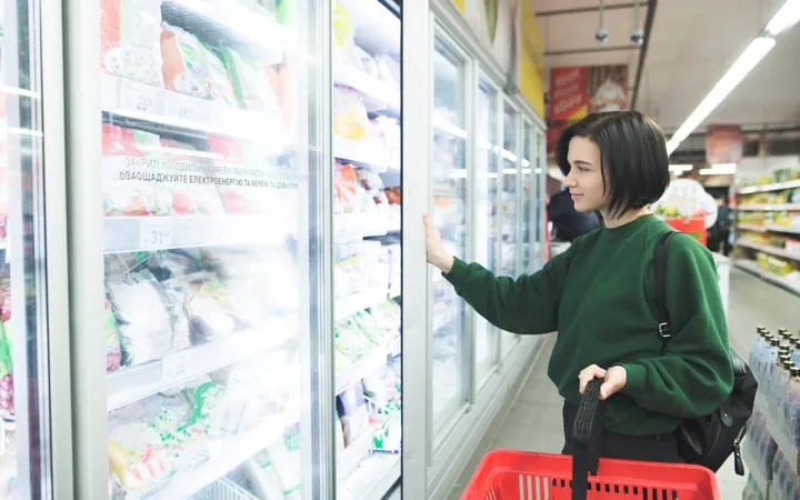 Frau mit kurzen Haaren steht im Lebensmittelgeschäft in der Tiefkühlabteilung und sucht sich etwas aus dem Gefrierschrank aus. Frau mit kurzen Haaren steht im Lebensmittelgeschäft in der Tiefkühlabteilung und sucht sich etwas aus dem Gefrierschrank aus.
