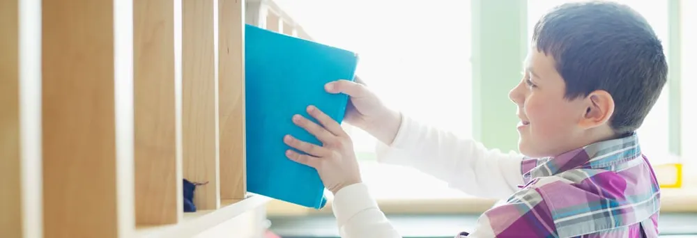 Junge stellt etikettierten Ordner ins Schulregal Junge stellt etikettierten Ordner ins Schulregal