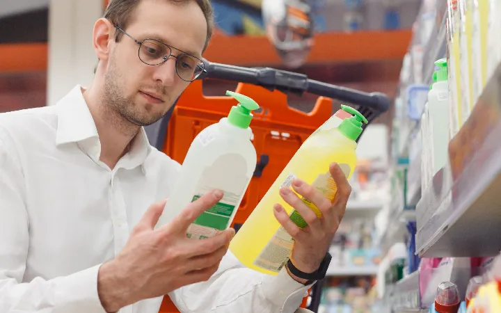 Mann vergleicht Produktinhalte anhand Etiketten Mann vergleicht Produktinhalte anhand Etiketten