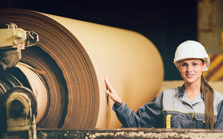 Frau steht neben Testlinerpapier-Rolle  Frau steht neben Testlinerpapier-Rolle