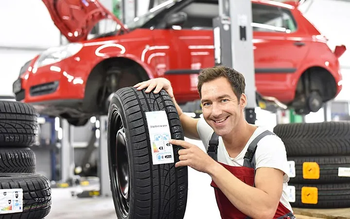 Mann in Werkstatt deutet auf Reifen-Etikett hin Mann in Werkstatt deutet auf Reifen-Etikett hin