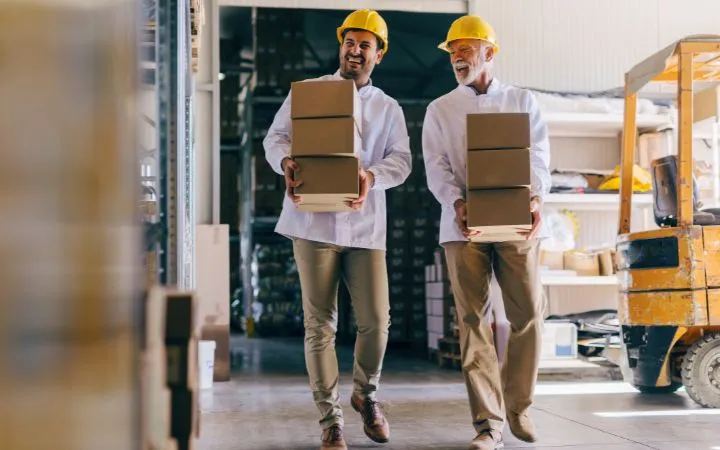Zwei Männer tragen Faltschachteln in Lagerhalle Zwei Männer tragen Faltschachteln in Lagerhalle
