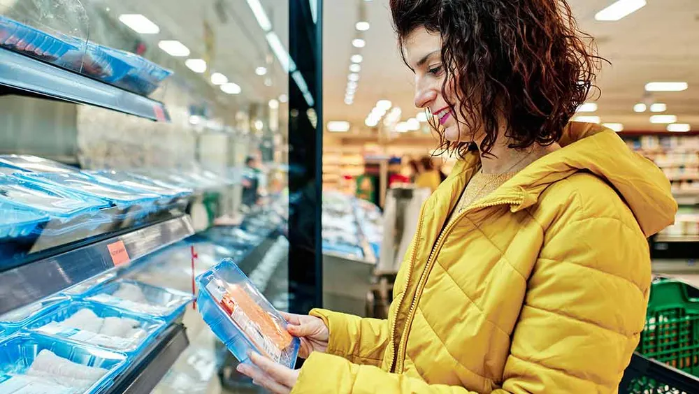 Frau liest Verpackung in der Kühlabteilung durch  Frau liest Verpackung in der Kühlabteilung durch