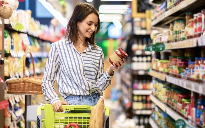 Frau in der Konservenabteilung mit einem Einkaufswagen am durchlesen eines Etiketts auf einer Konserve Frau in der Konservenabteilung mit einem Einkaufswagen am durchlesen eines Etiketts auf einer Konserve