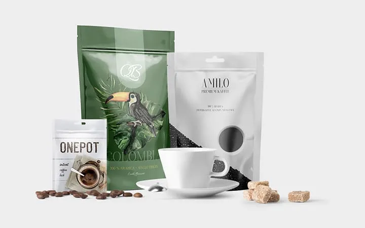 Drei Beutelverpackungen in unterschiedlichen Größen für Kaffeebohnen mit einer Kaffee Tasse   Drei Beutelverpackungen in unterschiedlichen Größen für Kaffeebohnen mit einer Kaffee Tasse